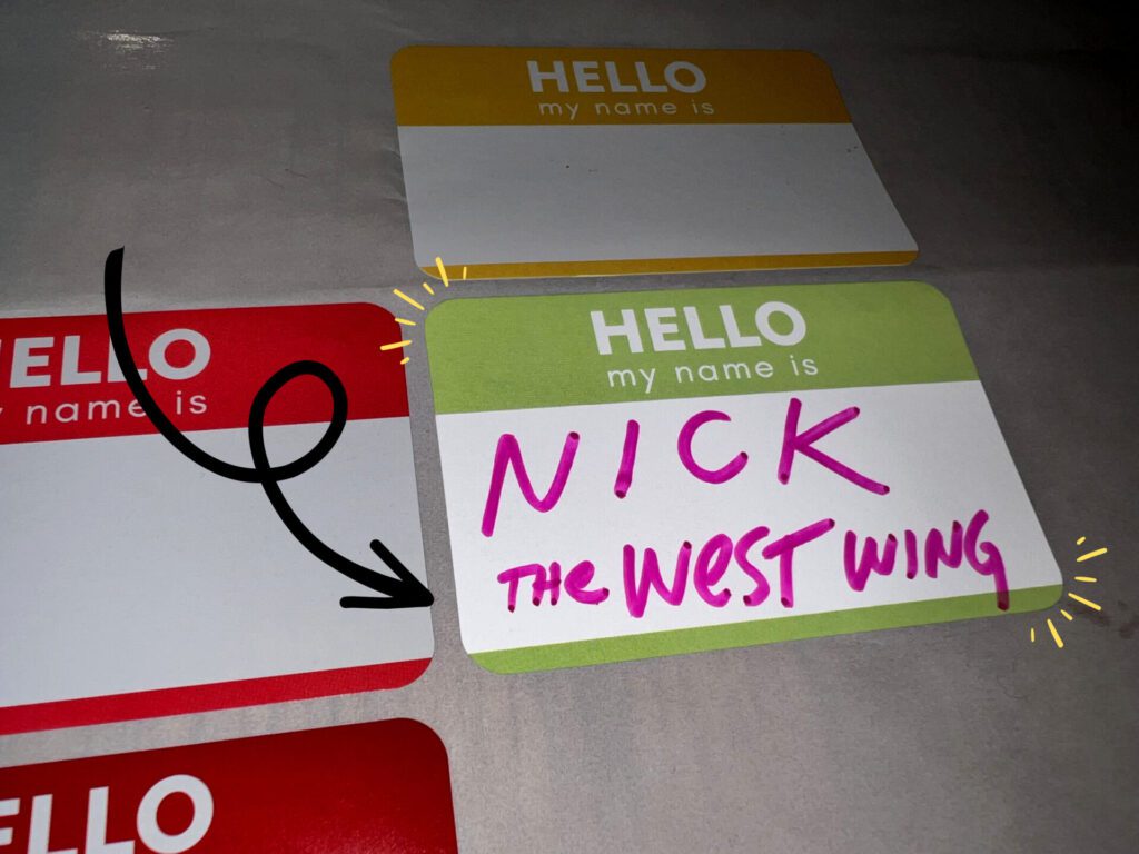 Name tags laid on the table with a handwritten text: "Nick The West Wing" with an arrow pointing to it and a two yellow starburst