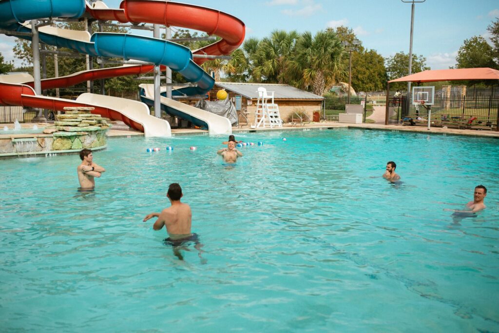 Men swimming in outdoor pool with slides in adult summer camp